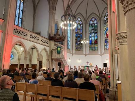 Innenraum der bunt beleuchteten Evangelischen Stadtkirche in Baden-Baden während des Aperol-Gottesdienstes am 13. September 2025. Die Besucher sitzen auf Holzbänken und blicken zum Altar, wo die junge Band der Petrusgemeinde Rastatt spielt.