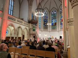 Quelle: Pfarrerin Mirjam Keim - eingebettet von kirchenbezirk-babara.de Innenraum der bunt beleuchteten Evangelischen Stadtkirche in Baden-Baden während des Aperol-Gottesdienstes am 13. September 2025. Die Besucher sitzen auf Holzbänken und blicken zum Altar, wo die junge Band der Petrusgemeinde Rastatt spielt.