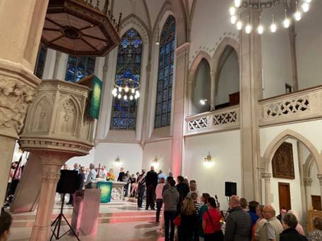 Innenraum der bunt beleuchteten Evangelischen Stadtkirche in Baden-Baden während des Aperol-Gottesdienstes am 13. September 2025. Die Gottesdienstbesucher stehen in einer Schlange, die zu dem Altar führt, neben dem sie ein Schnapsgläschen mit klassischem oder alkoholfreiem Aperol erhalten.